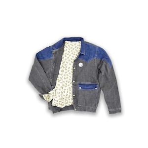 Puede incluir: Una chaqueta vaquera gris oscuro con un yugo de mezclilla azul y un forro estampado blanco. La chaqueta tiene cierre de botón y un solo bolsillo en el lado izquierdo.