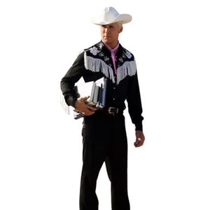 May include: A man wearing a black long-sleeved shirt with white fringe and embroidery, a pink neck scarf, and a white cowboy hat. He is holding a stack of books.