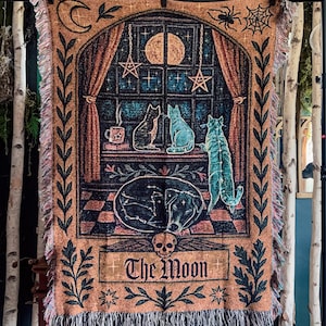 May include: A woven tapestry featuring a celestial design with cats, a dog, and the moon. The tapestry has a brown background with a window scene, stars, and the words "The Moon". The tapestry has a fringed edge.