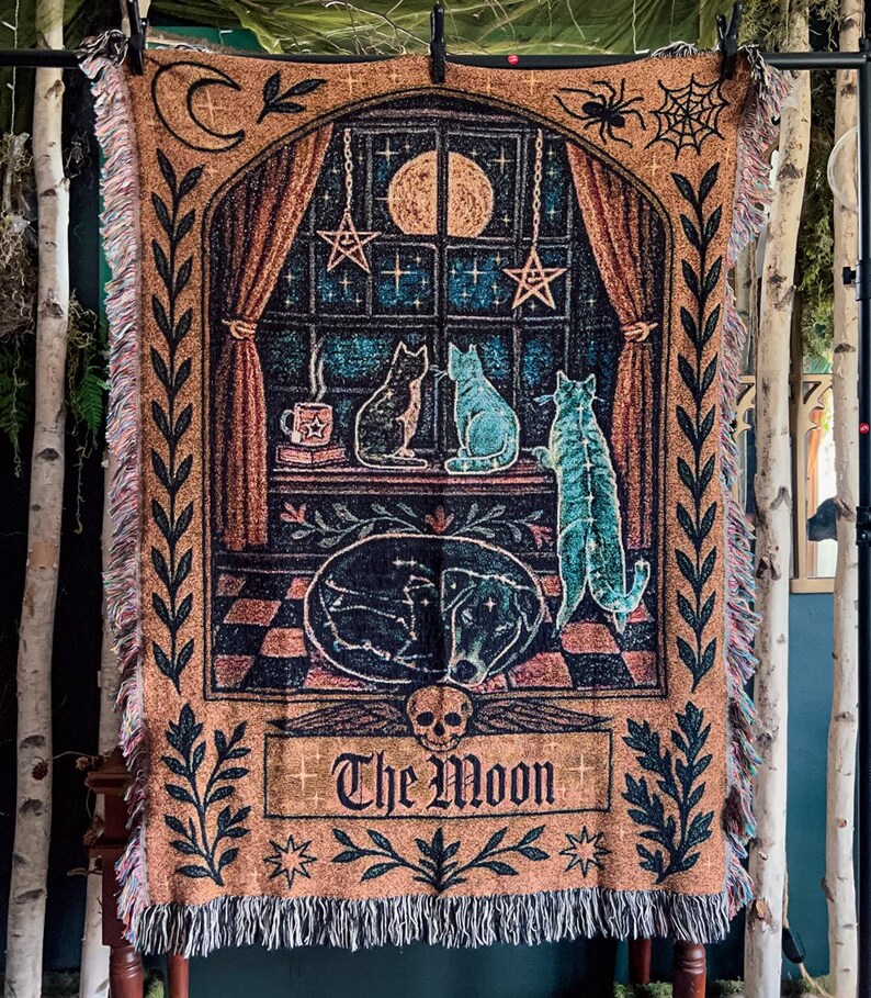 May include: A woven tapestry featuring a celestial design with cats, a dog, and the moon. The tapestry has a brown background with a window scene, stars, and the words "The Moon". The tapestry has a fringed edge.