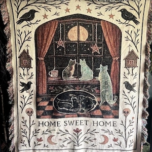 Könnte beinhalten: Gewebte Überwurfdecke mit einer skurrilen Szene mit Katzen, einem Hund und einem Vollmond. Das Design umfasst ein Fenster, Sterne und den Text "HOME SWEET HOME". Die Decke hat einen Fransenrand und einen cremefarbenen Hintergrund.