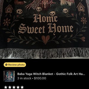 May include: A woven throw blanket featuring a dark forest scene with a central figure holding a broom, a fox, skulls, mushrooms, and two small houses on chicken legs. The text Home Sweet Home is centered in gothic font with a heart below the text.