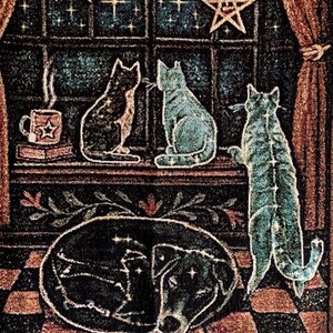 May include: A tapestry featuring a celestial theme with cats, a dog, and a skull. The cats are in shades of black and blue, with a dog depicted in an oval shape. Stars and moons adorn the background, with a cup of coffee on a shelf.