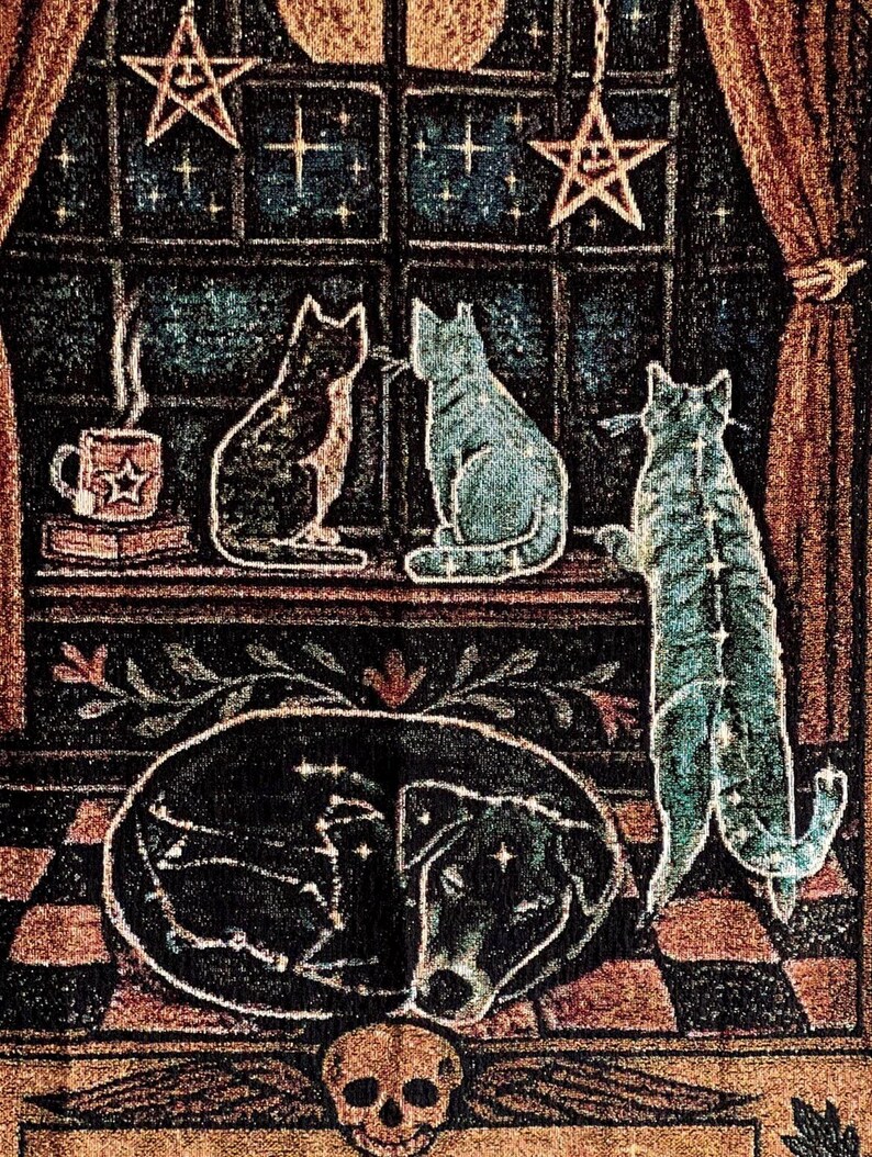 May include: A tapestry featuring a celestial theme with cats, a dog, and a skull. The cats are in shades of black and blue, with a dog depicted in an oval shape. Stars and moons adorn the background, with a cup of coffee on a shelf.