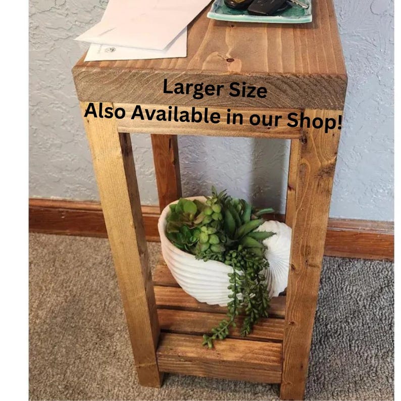 May include: A rustic, wooden side table with a lower shelf and a decorative white seashell-shaped planter filled with greenery. The table has the text "Larger Size Also Available in our Shop!"