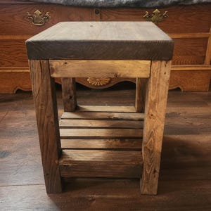 May include: A rustic wooden side table with a dark brown top and a lower shelf made of horizontal slats. The legs and frame are constructed from lighter-toned wood, showcasing natural grain patterns. The table is designed for indoor use.