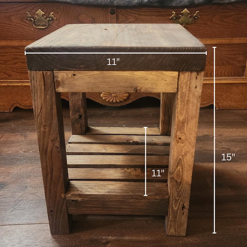 May include: A rustic wooden side table with a dark stained top. The table is 11 inches wide, 15 inches tall, and has a lower shelf. The wood has a natural, weathered appearance, showcasing the grain and knots. The design is simple and sturdy.