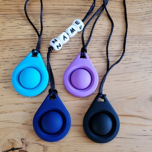 May include: Four silicone fidget toys in the shape of teardrops with a button in the center. The toys are blue, purple, dark blue, and black. The blue toy is attached to a black cord with white beads that spell "NAME".