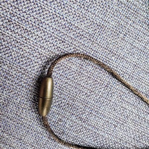 May include: A brown cord necklace with a magnetic clasp. The clasp is oval shaped and has a metallic finish.
