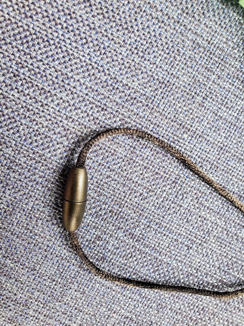 May include: A brown cord necklace with a magnetic clasp. The clasp is oval shaped and has a metallic finish.