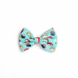 May include: A turquoise blue bow tie with a pattern of various sushi rolls. The sushi rolls are illustrated with smiling faces.