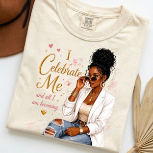 Può includere: Una t-shirt color crema con la grafica di una persona dai capelli ricci scuri che indossa occhiali da sole, un blazer bianco e jeans blu. Il testo recita I Celebrate Me and all I am becoming, decorato con cuoricini rosa e stelle dorate.
