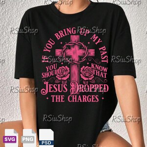 Può includere: T-shirt nero con croce rosa, rose e testo. Il testo recita: "YOU BRING MY PAST, YOU SHOULD KNOW THAT JESUS DROPPED THE CHARGES". La maglietta ha girocollo e maniche corte.