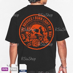May include: Black t-shirt with an orange graphic on the back. The graphic is a skull with a rose and the text "MAY THE BRIDGES I BURN LIGHT MY WAY" in a circular design. The shirt is a casual style.
