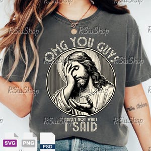 May include: Dark gray t-shirt featuring a distressed graphic of Jesus with his hand on his face, inside a circular frame. The text "OMG YOU GUYS" arches above the image, with "THAT'S NOT WHAT I SAID" below.