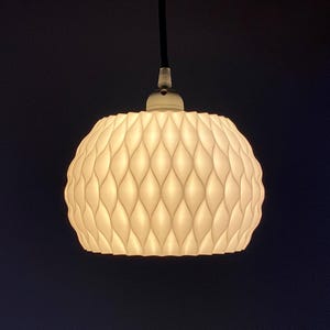 May include: A white, round, pendant light fixture with a textured, geometric pattern. The light is on and casting a warm glow.