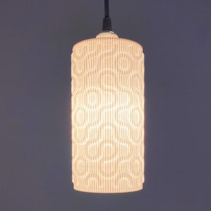 May include: A white pendant light fixture with a cylindrical shade featuring a textured pattern. The shade is illuminated with a warm white light.
