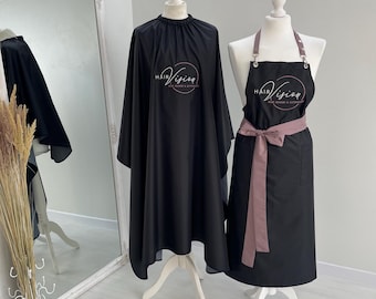 Könnte beinhalten: Ein schwarzer Friseurumhang und eine schwarze Schürze mit altrosa Trägern und Bindegürtel, beide mit dem weißen und altrosa kreisförmigen Logo-Schriftzug Hair Vision Hair Design & Extensions, präsentiert auf zwei weißen Schaufensterpuppen.