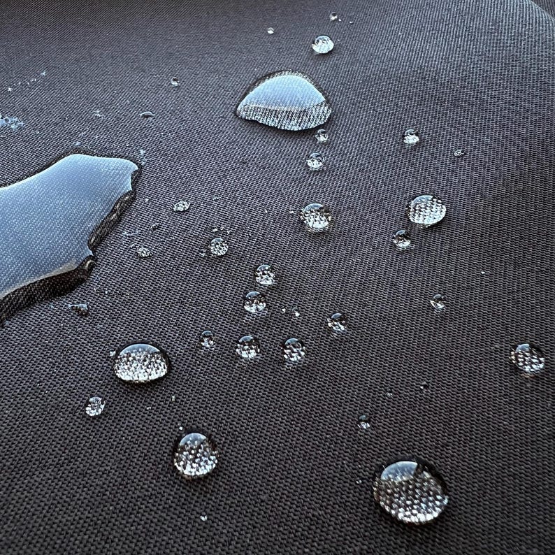May include: Close-up of a dark gray fabric surface with multiple water droplets, some of which are large and round, and others are smaller and more dispersed.