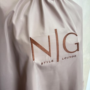 May include: A light brown hair cutting cape with the text "N|G STYLE LOUNGE" embroidered in brown on the front.