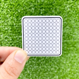 Puede incluir: Una pegatina blanca con un borde negro y una cuadrícula de 100 círculos pequeños.