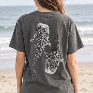 May include: A charcoal gray short-sleeve t-shirt featuring a white graphic print of two whale sharks on the back. The shirt has a crew neckline and a relaxed fit. The word PEPPER is printed in the upper left corner of the image.