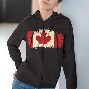 May include: Black zip-up hoodie with a distressed Canadian flag design. The flag features a red maple leaf on a white background, set against a red background. The hoodie has a full zip and a hood.