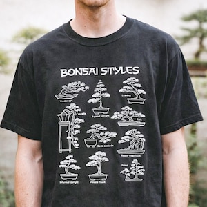 May include: A black short-sleeve t-shirt featuring a white graphic print titled Bonsai Styles. The design displays nine distinct bonsai tree illustrations with labels including Windswept, Formal Upright, Leaning, Cascade, Raft, Semi-cascade, Roots-over-rock, Informal Upright, Double Trunk, and Group.