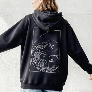 May include: Black hoodie with a white graphic of a wave and Fibonacci sequence design. The hoodie has a hood and long sleeves. The design is on the back of the hoodie.