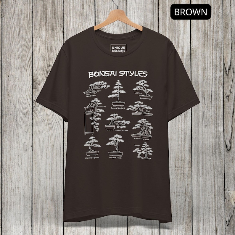 May include: A dark brown short-sleeve t-shirt featuring a white graphic print titled Bonsai Styles. The design displays nine distinct bonsai tree illustrations with labels including Windswept, Cascade, Formal Upright, Leaning, Raft, Semi-cascade, Root-over-rock, Informal Upright, Double Trunk, and Group.