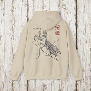 May include: Beige hoodie featuring a detailed black and white illustration of a praying mantis on the back. The design includes the Japanese characters for mantis in red. The hoodie has a hood and long sleeves.