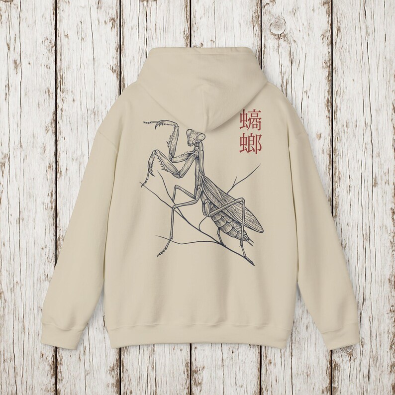 May include: Beige hoodie featuring a detailed black and white illustration of a praying mantis on the back. The design includes the Japanese characters for mantis in red. The hoodie has a hood and long sleeves.