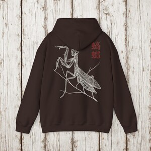 May include: A dark brown hoodie featuring a detailed white illustration of a praying mantis perched on a branch. The design includes the Chinese characters for mantis in red on the upper right. The hoodie has a hood and long sleeves.