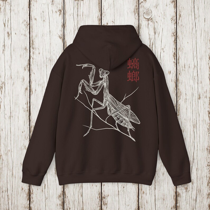May include: A dark brown hoodie featuring a detailed white illustration of a praying mantis perched on a branch. The design includes the Chinese characters for mantis in red on the upper right. The hoodie has a hood and long sleeves.
