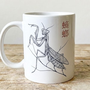 May include: White ceramic mug featuring a detailed black and white illustration of a praying mantis. The mug also has red Chinese characters. The mug has a white handle and is set against a wooden surface.