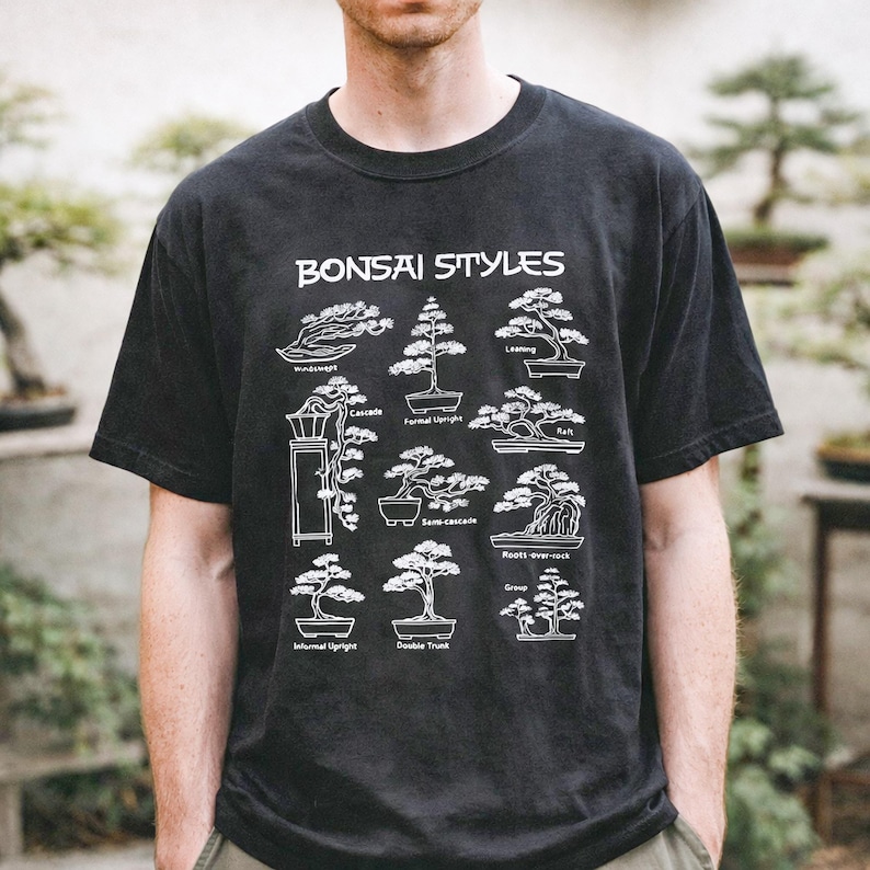 May include: A black short-sleeve t-shirt featuring a white graphic print titled Bonsai Styles. The design displays nine distinct bonsai tree illustrations with labels including Windswept, Formal Upright, Leaning, Cascade, Raft, Semi-cascade, Roots-over-rock, Informal Upright, Double Trunk, and Group.