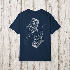 May include: Navy blue t-shirt featuring a white dotted illustration of two whale sharks. The design is on the back of the shirt. The shirt is made of a soft material.