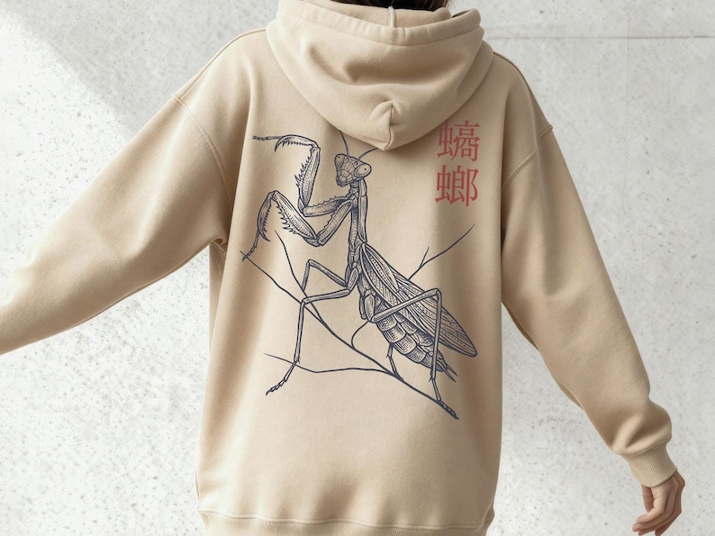 May include: Beige hoodie with a detailed black and gray illustration of a praying mantis on the back. The hoodie also features red Japanese characters. A comfortable, casual garment.