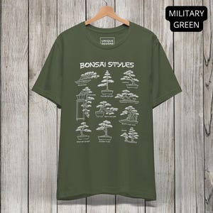 May include: A military green short-sleeve t-shirt featuring a white graphic print titled Bonsai Styles. The design displays nine distinct bonsai tree illustrations with labels including Wind-swept, Cascade, Formal Upright, Leaning, Raft, Semi-cascade, Roots-over-rock, Informal Upright, Double Trunk, and Group.