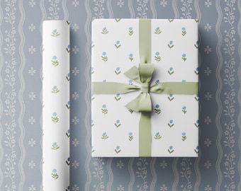 May include: White gift wrap with a repeating pattern of small blue flowers and green stems. A green ribbon is tied in a bow on top of the wrapped gift.