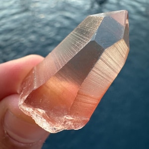 Może przedstawiać: Przezroczysty kryształ kwarcu z różowym odcieniem. Kryształ jest spiczasty z jednej strony i ma szorstką, naturalną fakturę.