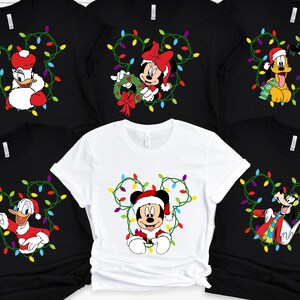 May include: Black and white t-shirts featuring Disney characters in Christmas attire. Mickey Mouse, Minnie Mouse, Donald Duck, Pluto, and Goofy are depicted with festive lights. The white shirt features Mickey Mouse.