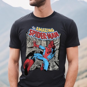 Puede incluir: Camiseta negra con una ilustraci&oacute;n de c&oacute;mic de Spider-Man. El dise&ntilde;o incluye el texto "the AMAZING SPIDER-MAN" en una fuente colorida. El superh&eacute;roe est&aacute; representado con su cl&aacute;sico traje rojo y azul.