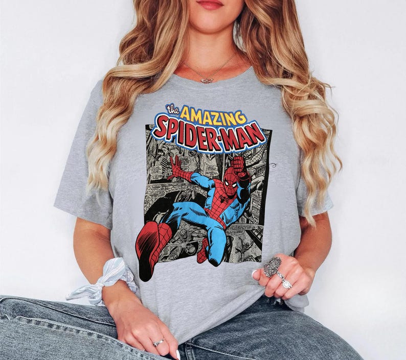 Puede incluir: Camiseta gris claro con un gr&aacute;fico de c&oacute;mic de Spider-Man. El gr&aacute;fico incluye las palabras "the AMAZING SPIDER-MAN" en amarillo y rojo. Spider-Man est&aacute; representado con su cl&aacute;sico traje rojo y azul.