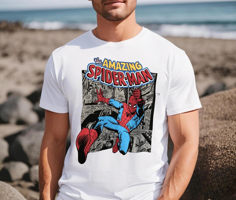 Puede incluir: Camiseta blanca con un gr&aacute;fico de c&oacute;mic de Spider-Man. El dise&ntilde;o incluye el texto "The Amazing Spider-Man" en amarillo y rojo. El superh&eacute;roe est&aacute; representado en su traje rojo y azul, en una pose din&aacute;mica.