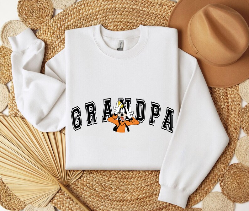 May include: White sweatshirt with the word "GRANDPA" in black block letters with a cartoon character in the center. The cartoon character is wearing an orange shirt and a yellow hat.