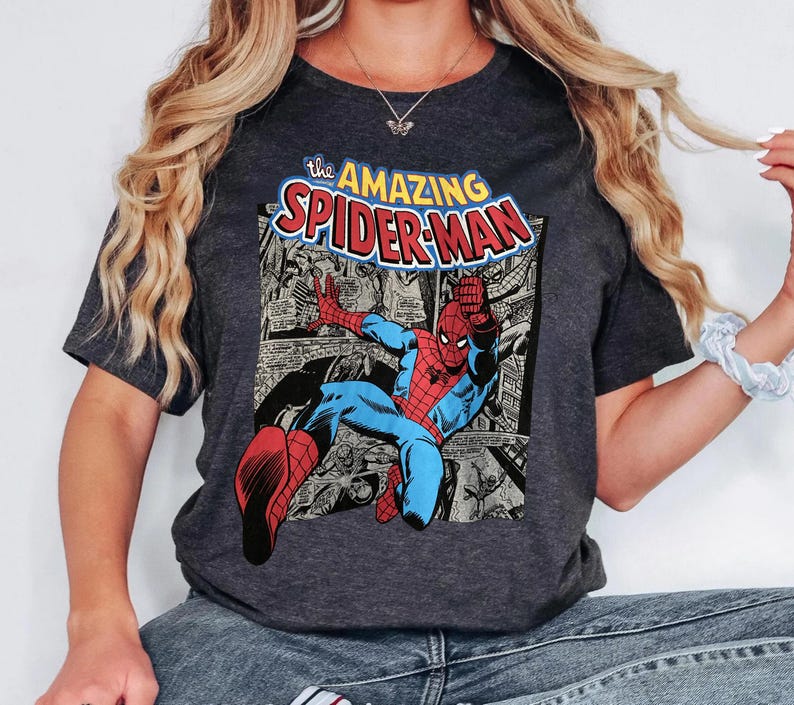 Puede incluir: Camiseta gris oscuro con un gr&aacute;fico de c&oacute;mic de Spider-Man en acci&oacute;n. El gr&aacute;fico incluye el texto "the AMAZING SPIDER-MAN" en amarillo y rojo. La camiseta tiene cuello redondo y mangas cortas.