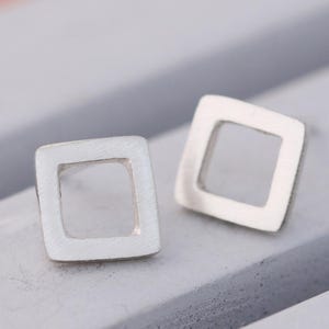 Square stud earrings in silver and black finishes on grey dish, minimal earrings
