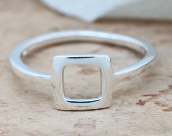 May include: A silver ring with a square design. The ring features a thin band that leads to a square-shaped centerpiece with an open center. The ring is made of a shiny, reflective metal.