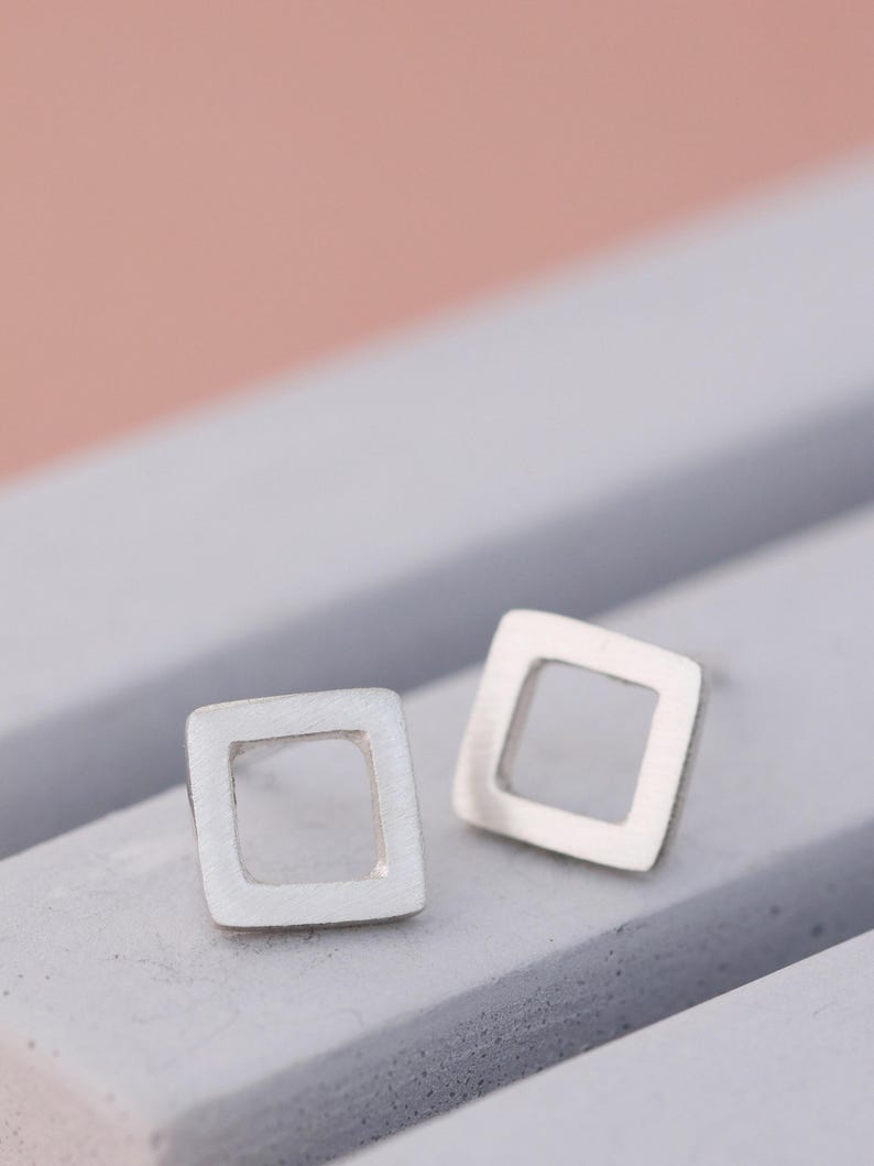 Square stud earrings in silver and black finishes on grey dish, minimal earrings